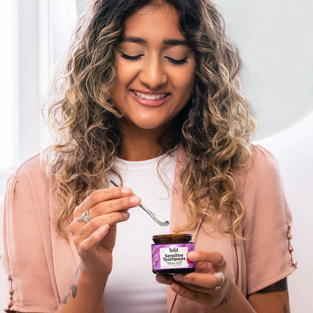 Our Values | Solid Oral Care Person smiling with toothpaste in a jar and toothpaste scoop